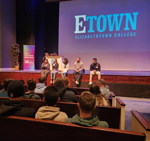 group of students sitting on edge of stage talking to seated audience