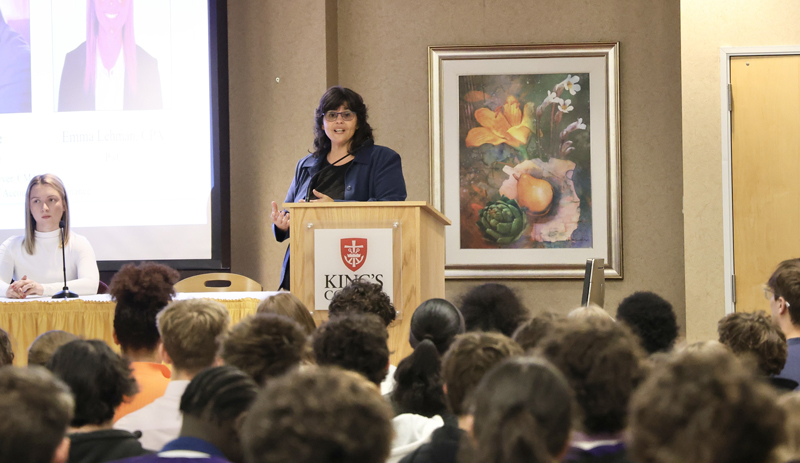A speaker at a podium with King College banner speaking before a room of students