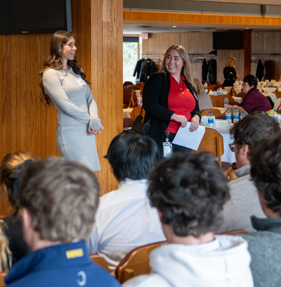 Two female speakers standing before a group of seated students