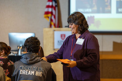 smiling woman handing paper to student in an auditorium