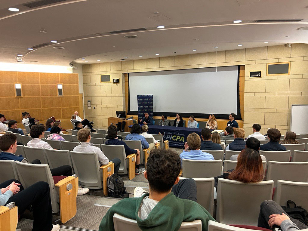 students in auditorium viewing speaking panel