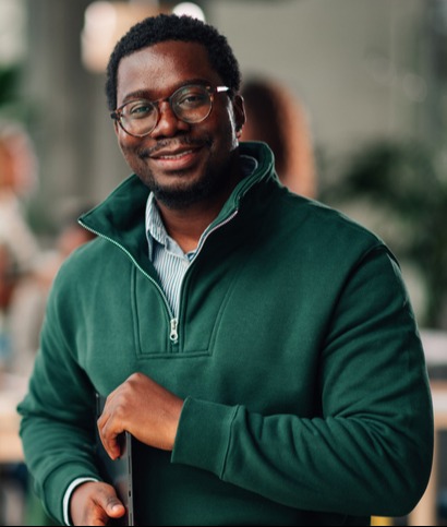 Black man holding laptop with people at table in background