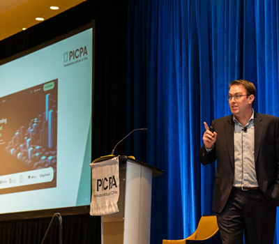 am24-11 Speaker behind a podium showing a slide on screen