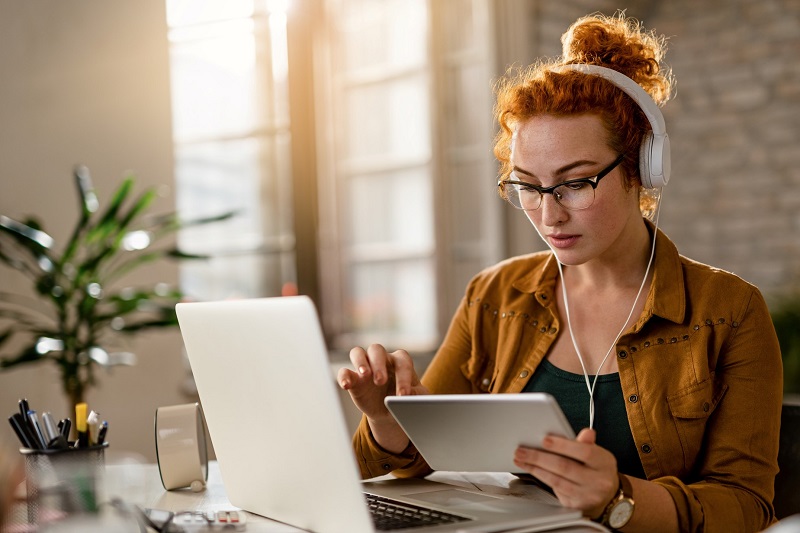 Young woman at desk with headphones and laptop.
