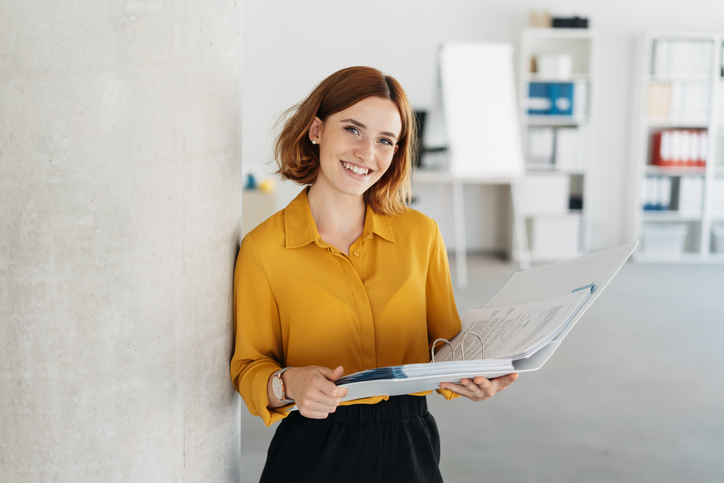 Smiling woman in mustard yellow shirt holding a binder