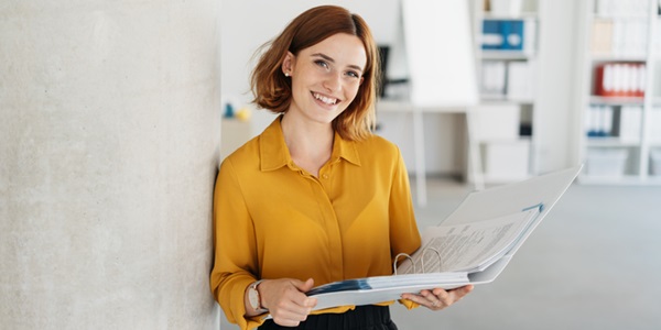 woman in office Smiling woman in mustard yellow shirt holding a binder