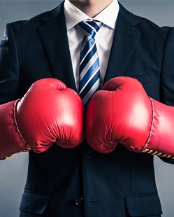 Man in business suit wearing large red boxing gloves