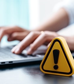 Yellow "warning" triangle on desk with someone using laptop